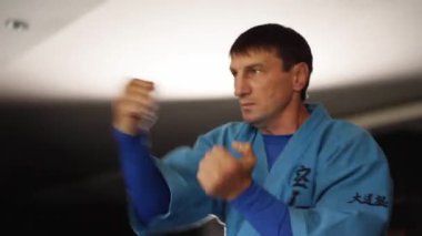 Martial arts man in kimonos practices kicks and punches. Male fighter wearing kimono training at gym. Kick boxer jumping and practicing kicking and punching actions indoors. People and sport concept