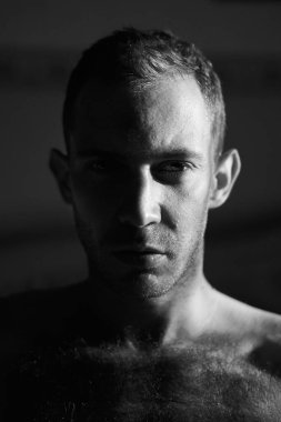 Kameraya bakan sert ışıklı yakışıklı adamın portresi. Çekici erkek yüzünün yarısı güneşin doğuşuyla aydınlanır. Yüksek kaliteli siyah beyaz fotoğraf