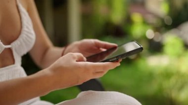 Unrecognizable woman using smart phone texting with AI, surfing social media, checking news, playing mobile games or texting messages sitting otside. Female spends time with cell gadget close-up