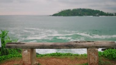 Young blonde woman walks to bench with spectacular view of ocean, sits down with her her back towards camera slow motion. Pretty girl approaches bench at scenic location and sits enjoying view