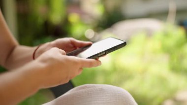 Unrecognizable woman using smart phone texting with AI, surfing social media, checking news, playing mobile games or texting messages sitting otside. Female spends time with cell gadget close-up