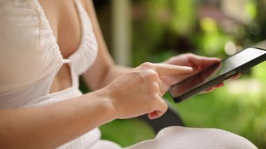 Unrecognizable woman using smart phone texting with AI, surfing social media, checking news, playing mobile games or texting messages sitting otside. Female spends time with cell gadget close-up