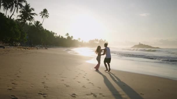若い幸せなカップルが手を取り合って走り 夏のバックビューを楽しんで一緒にビーチで遊んでいます ボーイフレンドレイジングと回転ガールフレンド持っています楽しいです海辺で日の出 — ストック動画