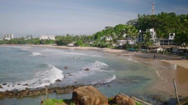 Ocean view with waves running, rocks and a green island in the background. Sea expanse landscape. Beautiful blue sea and large calm waves float on the Indian Ocean. Ocean and sky background landscape