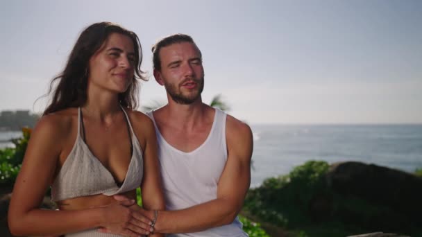 Young Multiracial Couple Sitting Seaside Huhhing Smiling Looking Aside Pointing — Stock videók