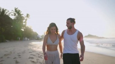 Young biracial happy couple hugging and walking on the beach together enjoying summer. Cheerful boyfriend and girlfriend relaxing and taking walk at seaside embracing at sunrise.