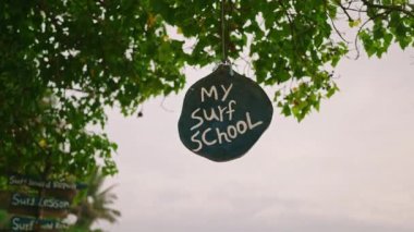 Surf school wooden sign on beach. Black handmade sign near sea. Crafted surfing sign hang by ocean in tropical location. Surfing concept. acation concept. Closeup shot