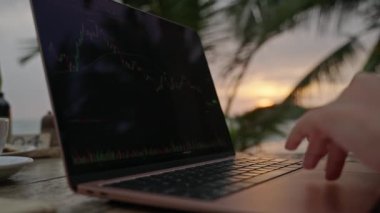 Bilgisayardaki kadın kripto para tüccarı günbatımında açık deniz kafesinde çalışan online haritaları kontrol ediyor. Kadın kripto komisyoncusu okyanusa yakın plandaki borsa oranlarının grafiklerini analiz ediyor.