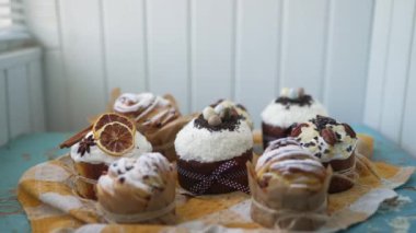 Traditional Easter cakes creatively decorated with white icing, candied fruits, nuts and chocolate on old wooden table. Stylish authentic Easter buns on a checked yellow tablecloth in rustic location
