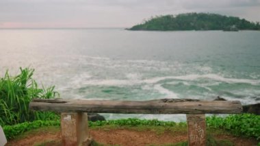 Uzun kıvırcık saçlı, uzun kıvırcık saçlı romantik bir kadın okyanus manzaralı bankta yürür, karamsar günbatımında sırtını kameraya yaslar. Kız manzaralı iyileşme yerine geliyor.