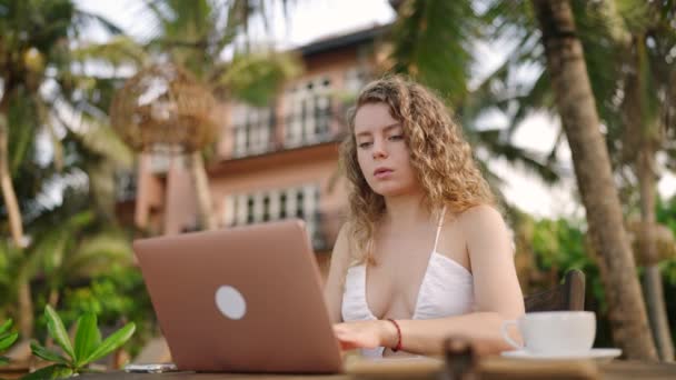 在海洋边的笔记本电脑上工作的年轻女性开发人员 室外热带咖啡店的女自由撰稿人 白人女孩在异国他乡的电脑上远程打字 全球工作概念 — 图库视频影像