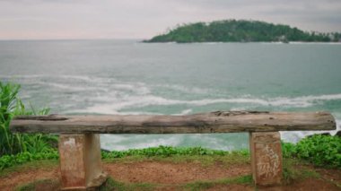 Young blonde woman walks to bench with spectacular view of ocean, sits down with her her back towards camera slow motion. Pretty girl approaches bench at scenic location and sits enjoying view