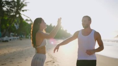 Young happy couple holding hands and running and fooling around on the beach together enjoying summer back view. Boyfriend and girlfriend having fun at seaside chasing each other at sunrise.