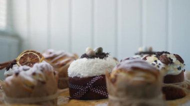 Traditional Easter cakes creatively decorated with white icing, candied fruits, nuts and chocolate on old wooden table. Stylish authentic Easter buns on checked tablecloth in rustic location closeup
