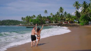 Dalgalar halinde okyanus akıntısı boyunca el ele koşan mayolu neşeli çift yavaş çekim yapıyor. Çok ırklı mutlu erkek ve kadın yavaş çekimde denizde neşeyle koşar.