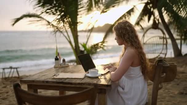 ラップトップの女性暗号トレーダーは 屋外の熱帯海辺のカフェでリモートで働いているキャンドルスティックチャートをオンラインでチェックします 女性ブローカー分析為替レートと海洋閉鎖による暗号株式への賭け — ストック動画