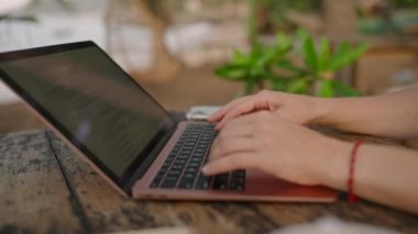 Hands of young woman coding on laptop in outdoor seaside cafe. Female freelancer typing on computer at tropical location by ocean. Young adult works remotely on exotic island. Worldwide work concept