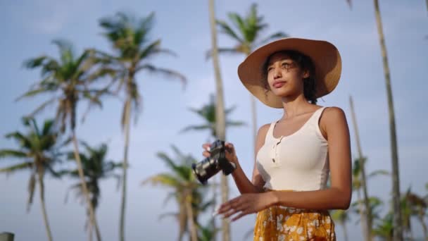 アフリカ系アメリカ人の女性は熱帯の島でカメラで写真を撮る 女性の多人種写真家観光客は休暇中に海の景色の場所を探索します 黒女の子取る写真上の日の出でわら帽子 — ストック動画