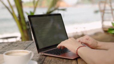 Laptopla çalışan genç bir kadın doğada açık bir kafede oturuyor. Tropikal bölgede bilgisayarda yazan serbest çalışan bir kadın. Genç yetişkinler egzotik yerlerde çalışırlar. Menüde yemek seçerler.