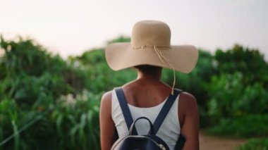 Afrika kökenli Amerikalı kadın tropik adada sırt çantasıyla yürüyüş yapıyor. Hasır şapkalı çok ırklı kadın deniz kenarında yürüyor. Siyah güzel kız okyanus kıyısını keşfediyor. Arkadan bak. Seyahat tatilinde turist gezisi.