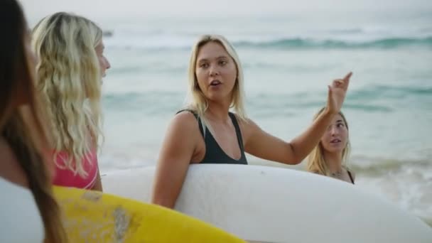 日の出にビーチを歩く幸せな多人種のサーファーの女の子 夜明けにビーチを歩くサーフボードを運ぶ陽気な出産の女性サーファー 若いサーフィンの女性が歩いて海潮で話をする — ストック動画