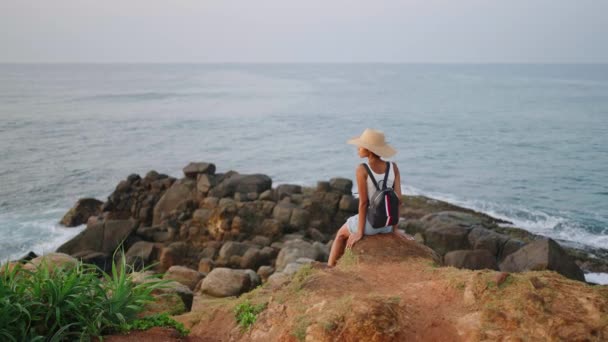 美しいアフリカの女性は日の出に島に立つ海の景色を楽しんでいます エキゾチックな海の目的地への旅行にわら帽子の観光で出産の女性 観光客の二人組の女の子は岩だらけの崖の上に座ってリラックス — ストック動画
