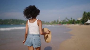 Çok ırklı siyahi kadın, okyanus sahillerinde egzotik adalarda tropik tatillerde koşuyor. Afrika kökenli Amerikalı kadın dönüyor, şapkasıyla deniz kıyısında koşuyor. Bipoc seyahat turunda eğleniyor. Beni takip et.