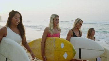 Mutlu çok ırklı sörfçü kızlar gün doğumunda sahilde yürüyor. Şafakta sahilde sörf tahtası taşıyan neşeli, çok ırklı kadın sörfçüler. Genç sörfçü kadınlar okyanus gelgitlerinde yürüyüp konuşurlar.