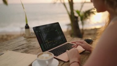 Bilgisayardaki kadın kripto para tüccarı günbatımında açık deniz kafesinde çalışan online haritaları kontrol ediyor. Kadın kripto komisyoncusu okyanusa yakın plandaki borsa oranlarının grafiklerini analiz ediyor.