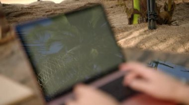 Modern laptop on tropical beach background with palm trees reflection on screen trees closeup. Blue sky and coconut palmtree leaves reflecting on computer screen. Online work, internet surfing