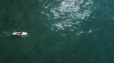 Genç bayan sörfçü güneşli bir günde, hava manzaralı tropik sahilde kristal okyanus suyunda sörf tahtasında kürek çekiyor. Sörfçü kız yaz tatili drone çekimlerinde kürek çekmekten ve sörf yapmaktan hoşlanıyor..