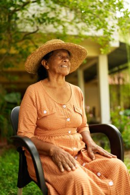 Arka planda bahçeli mutlu bir Hintli kadın çiftçinin portresi. Kıdemli Sri Lankalı neşeli kadın meyve bahçesinde kameraya bakıp yakından gülümsüyor. Çiftçilik ve bahçecilik kavramı