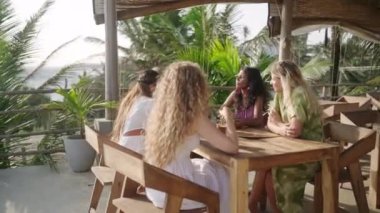 Seaview Restoran 'daki çeşitli kadınlar menüyü okuyor. Çok ırklı genç dişiler tropikal okyanus manzaralı bir kafede masada oturur sohbet eder, gülümser, yemeği seçer. Çok ırklı kadınlar yemek yer. Çeşitli arkadaşlıklar