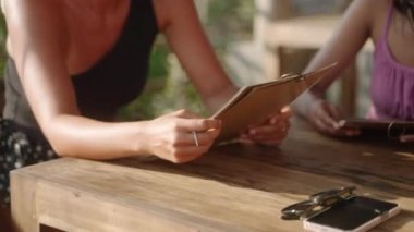 Kadın, tropik bir restoranın yakın planında restoran menüsü okuyor. Deniz kenarındaki kafede menüyü tutan kadınlar sayfaları çevirir, yiyecek ve içecekleri seçer. Serinletici ve içecek seç. Aperatifleri seçin