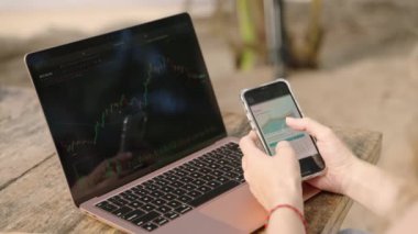 Akıllı telefondan istatistik çizelgelerini kontrol eden dizüstü bilgisayarı olan bir kadın kripto simsarı. Şifreli para birimleriyle çalışan serbest çalışan bir kadın telefonda diyagramları kontrol ediyor. Şifreleme grafiklerini yakından inceleyen kadın analist