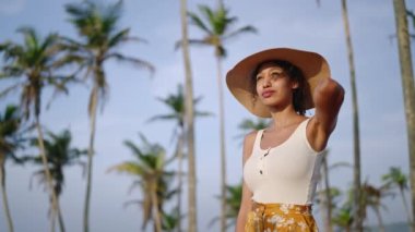 Afrikalı Amerikalı kadın tropikal adada kamerayla fotoğraf çekiyor. Kadın çok ırklı fotoğrafçı tatilde okyanus manzaralı yerleri keşfediyor. Siyah kız güneşin doğuşunda hasır şapkayla fotoğraf çekiyor.