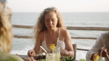 Çatal ve bıçakla deniz manzaralı çatı restoranında yemek yiyen bir kadın. Genç beyaz kadın arkadaşlarıyla otantik tropikal açık kafede vegan yiyecekler yiyor. Beyaz kız sağlıklı yemeğin tadını çıkarıyor..