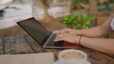 Genç bayan müteahhitin elleri dizüstü bilgisayarla okyanus kenarında çalışıyor. Açık hava tropikal kafede tanımlanamayan serbest çalışan kadın. Kafkasyalı bir kız egzotik mekanlarda bilgisayarla uzaktan kumandayla çalışıyor..