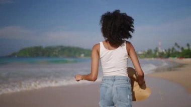 Çok ırklı siyahi kadın, okyanus sahillerinde egzotik adalarda tropik tatillerde koşuyor. Afrika kökenli Amerikalı kadın dönüyor, şapkasıyla deniz kıyısında koşuyor. Bipoc seyahat turunda eğleniyor. Beni takip et.