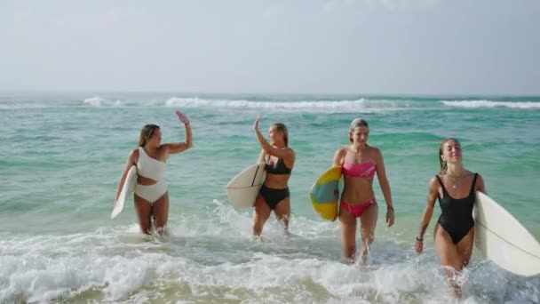 在阳光明媚的日子里 穿着比基尼的快乐的女冲浪者背着冲浪板在热带海滩上跑出了水面 穿着泳衣 快乐而又多姿多彩的女孩们在暑假里尽情享受水上运动的乐趣 — 图库视频影像