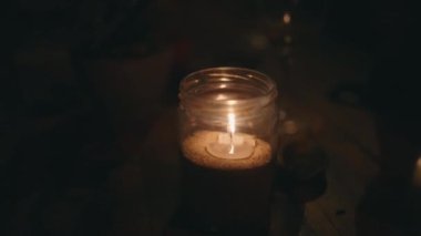 Karanlıkta cam kavanozda yanan mum ahşap masada. Meditasyon için mum alevinin rahatlatıcı rahat videosu. Karanlıkta titreyen sıcak alevler