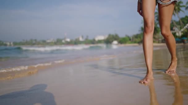 沿着海浪在奇异的岛屿上行走在沙滩上的黑人妇女的脚 深色皮肤的女性腿通过冲浪线 触摸白色泡沫 比波克女孩放松热带旅行到豪华度假胜地 — 图库视频影像