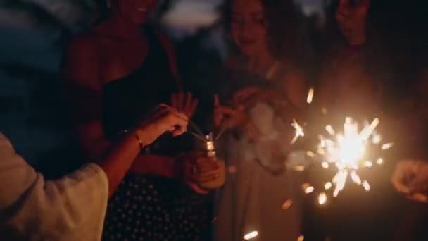 様々な女性が踊り 日没時に海辺の熱帯のパーティーでキラキラと笑います 7月4日独立記念日に輝く光で海で楽しむ若い笑顔の多人種女性 — ストック動画