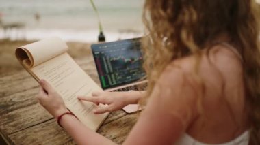Açık hava tropikal kafe menüsünde dizüstü bilgisayarı olan serbest çalışan bir kadın. Tatil köyünde uzaktan çalışan genç bir kadın menüyü seçerken kontrol ediyor. Tatil köyünde çalışan kadın kripto tüccarı.