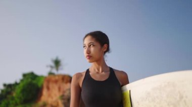 Okyanus sahilinde sörf tahtasıyla yürüyen Afrikalı Amerikalı kadın. Siyah kadın sörfçü sörf tahtasıyla gidiyor. Çok ırklı güzel bir kız gün doğumunda sörf yapmaya gidiyor. Ağır çekim, Slomo..