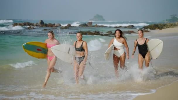 阳光明媚的日子 穿着比基尼的快乐的女冲浪者背着冲浪板在热带海滩上沿着海潮奔跑 在暑假里 穿着泳衣 喜欢水上运动的快乐女孩们沿着大海奔跑 — 图库视频影像