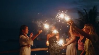 Çeşitli kadınlar gün batımında deniz kenarındaki tropik bekarlığa veda partisinde havai fişeklerle dans eder, güler. Gülümseyen çok kültürlü genç kadınlar 4 Temmuz Bağımsızlık Günü 'nde deniz kenarında ışıltılı ışıklarla eğleniyorlar.
