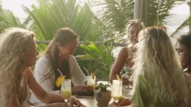 Brunch 'ta deniz manzaralı bir restoranda çok ırklı bayan arkadaşlar sohbet edip kokteyl içiyorlar. Tropikal okyanus manzaralı kahkahalar ve yudumlanmış içecekler masasında oturan çok ırklı ve neşeli kızlar.
