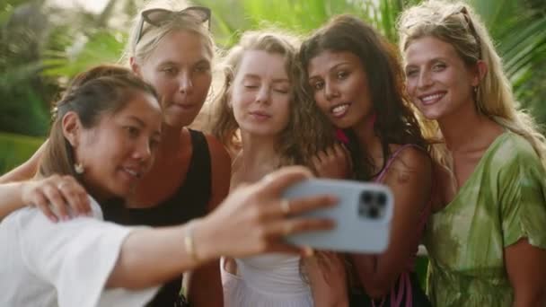 陽気多人種の女の子は休暇に自撮りを取ります 多様な若い女性がスマートフォンで自画像を撮る 多民族の幸せな女性の友人は エキゾチックな場所で笑顔と笑いの写真を撮る — ストック動画