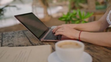 Genç bayan müteahhitin elleri dizüstü bilgisayarla okyanus kenarında çalışıyor. Açık hava tropikal kafede tanımlanamayan serbest çalışan kadın. Kafkasyalı bir kız egzotik mekanlarda bilgisayarla uzaktan kumandayla çalışıyor..